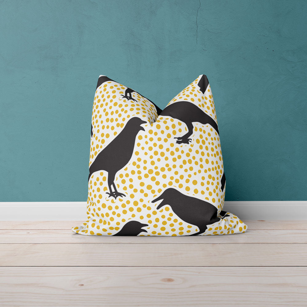 White pillow with yellow dots and black crows against a teal wall on a wood floor