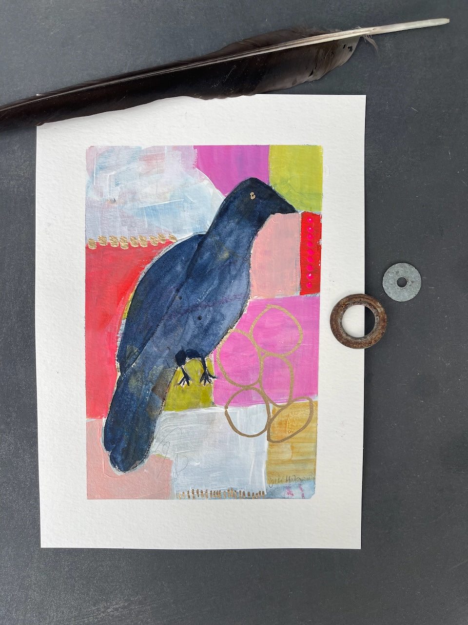 flat lay of a pink and orange crow painting with a feather and two shiny objects