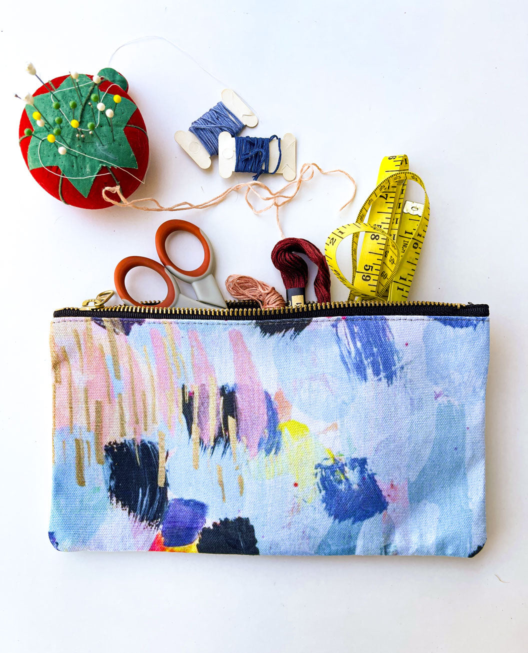 flat lay of pale blue zipper pouch with abstract brush strokes and sewing supplies